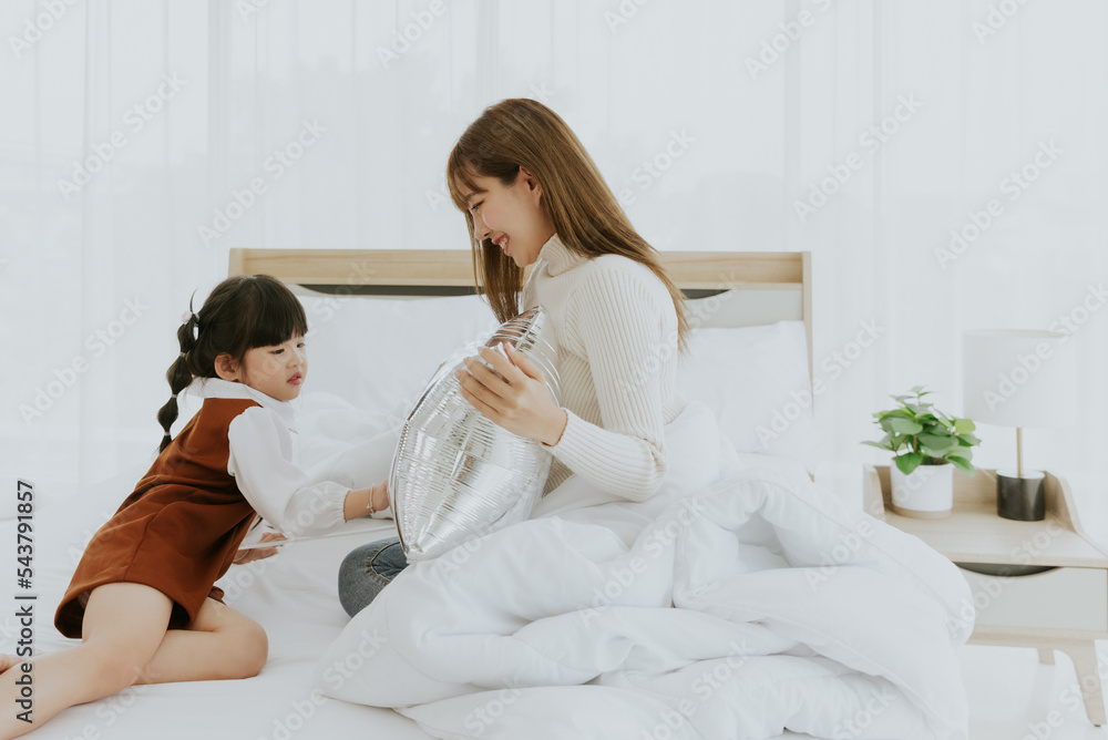 Young asian mother and 4years old kid daughter lying smiling and playing balloon together on white bed, Happy lovely family concept Young asian mother and 4years old kid daughter lying smiling and playing balloon together on white bed, Happy lovely family concept