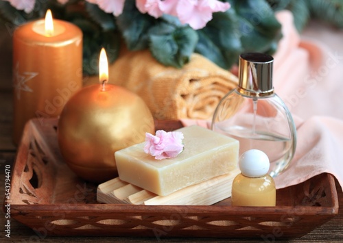 Spa concept with candles in gold and pink. Handmade olive soap, facecloth, towel, candles and pink cyclamen on wooden table.