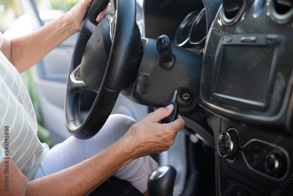 Close-up on senior woman in t-shirt entering her car. With one hand woman is holding the key and with other the steering wheel.
