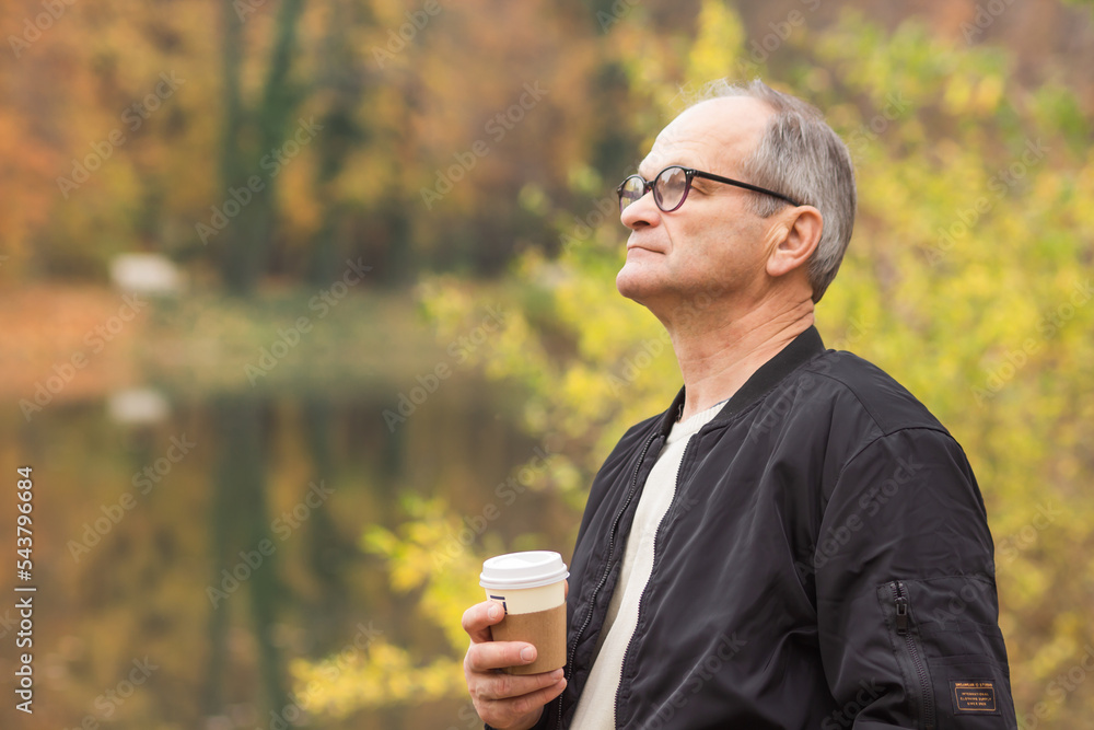 Senior man walking and drinking hot coffee in autumn city park. Elderly man holding disposable paper cup in his hands. Senior man walking and drinking hot coffee in autumn city park. Elderly man holding disposable paper cup in his hands.