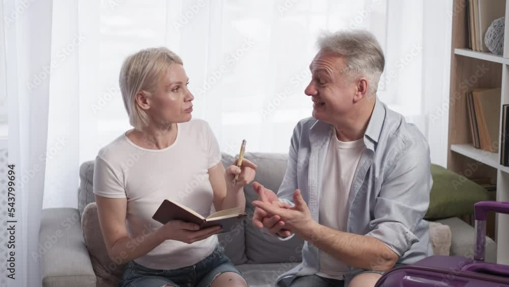 Vacation excitement. Inspired couple. Trip planning. Middle-aged happy man and woman making notes sitting home with suitcase light room interior. Vacation excitement. Inspired couple. Trip planning. Middle-aged happy man and woman making notes sitting home with suitcase light room interior.