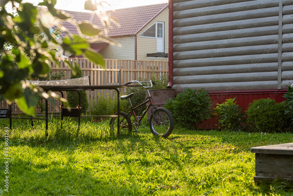 in the rays of the sun, a children's bicycle on the grass parked near the tennis table of a country house.