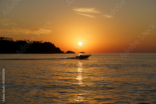 Sunset with a yacht on the tropical mediterranean sea. Evening or morning landscape with beautiful orange sun, calm water and soft light in summer
