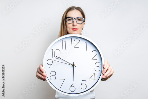 Photos Young woman in glasses holding a wall clock on a light background