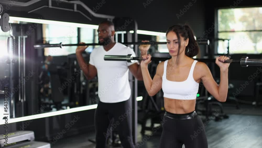 Attractive sports people, african man and caucasian woman, are working out with barbells at gym. Attractive sports people, african man and caucasian woman, are working out with barbells at gym.
