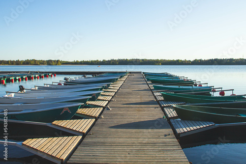 There are many rowboats at the pier.Sunset in the background. There is a calm on the lake