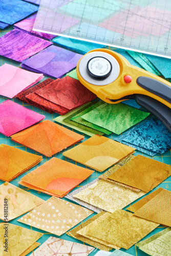 Pile of colorful fabric diamonds on cutter mat, quilting accessories