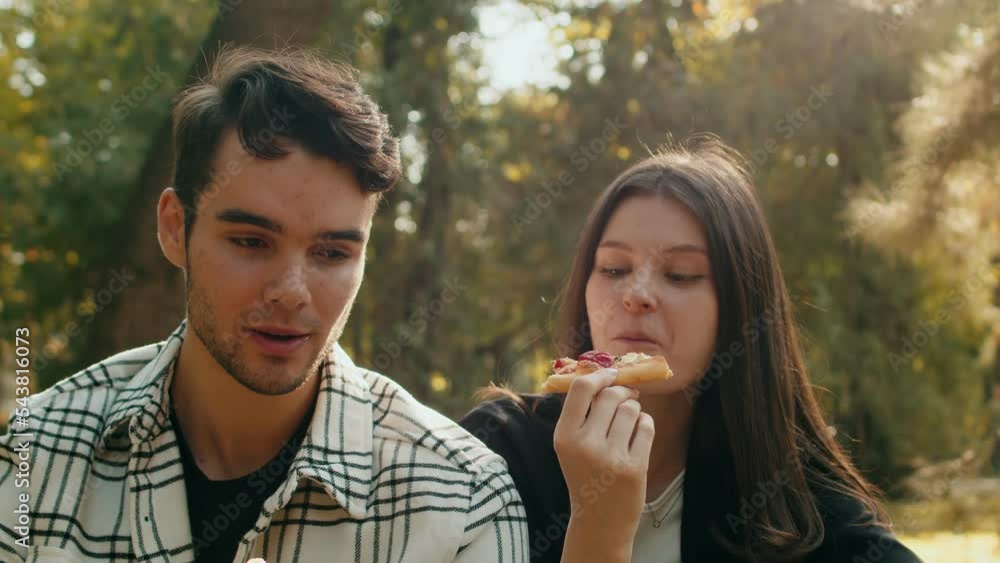 Beautiful couple of lovers enjoying tasty fast food pizza in the green park. Man and woman having a fun romantic picnic in nature during a sunset Beautiful couple of lovers enjoying tasty fast food pizza in the green park. Man and woman having a fun romantic picnic in nature during a sunset