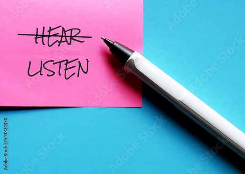 Pen and pink note on blue background with handwritten text HEAR changed to LISTEN, concept of practice active listening , focus and try to understand what speaker really want to communicate photo
