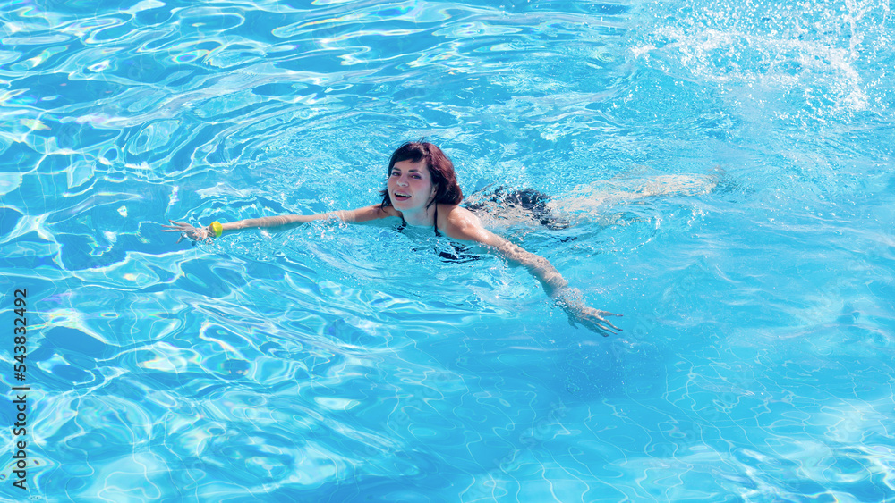 Young brunette woman swims blue water of the pool.