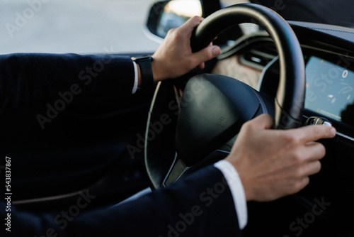 Side view of confident and handsome businessman in formal wear driving his car. Business trip. Caucasian businessman driving himself to work. Hands are on steering wheel