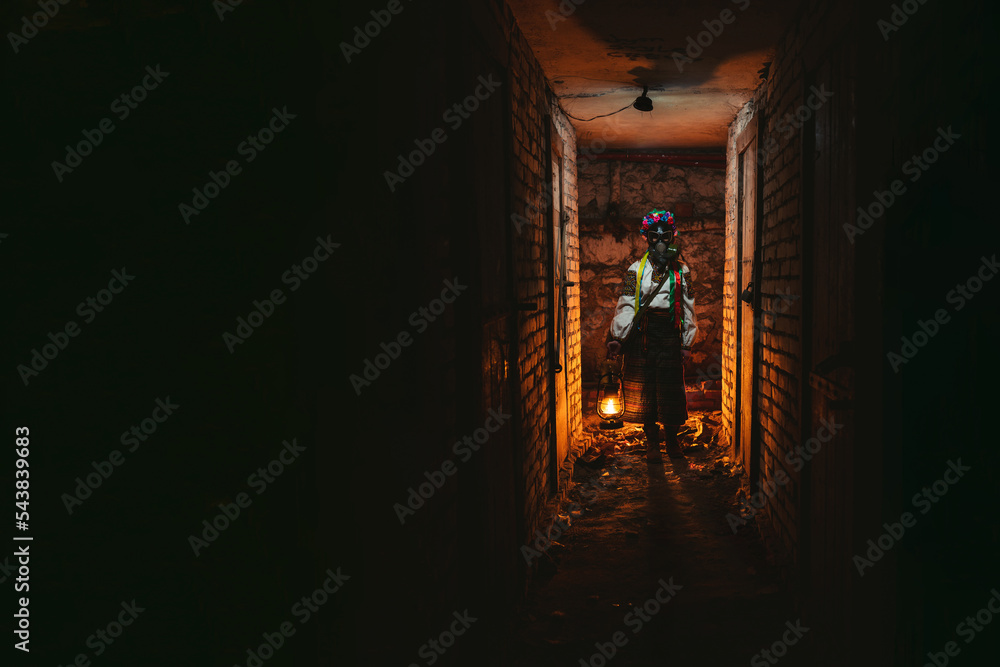 Ukrainian woman in a gas mask lights the way with an old gas lamp. Dressed in a traditional folk costume. They hide in the basement bomb shelters from chemical attacks, with poisonous gases, radiation
