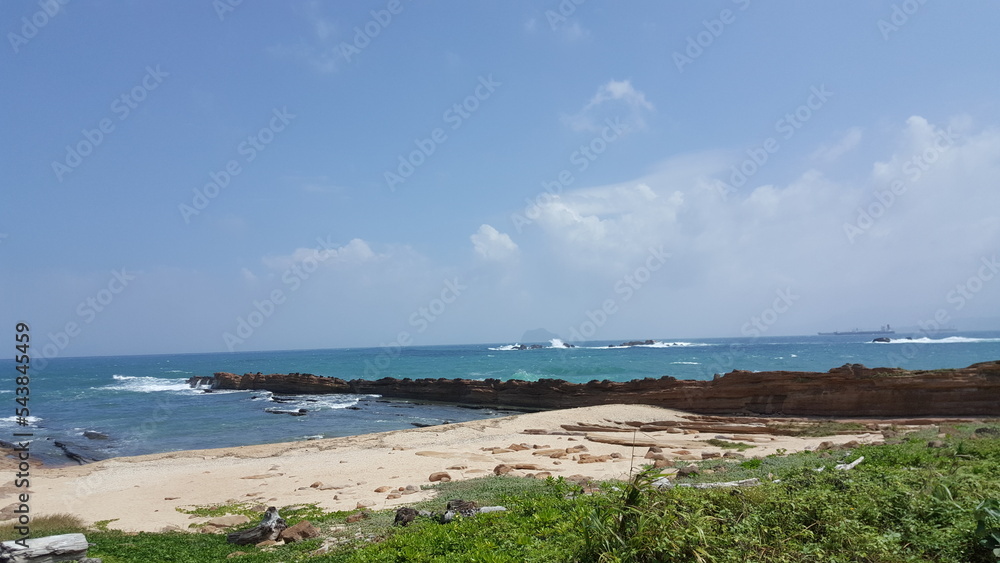 Taiwan. Blue ocean and blue sky with green grass. Sand and rocks.