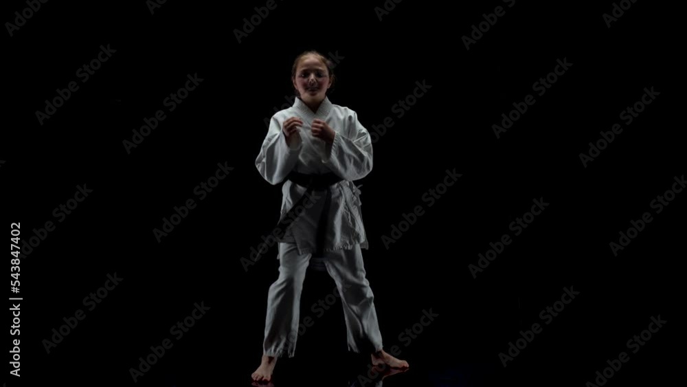 Young girl wearing kimono and practicing karate against black background Young girl wearing kimono and practicing karate against black background