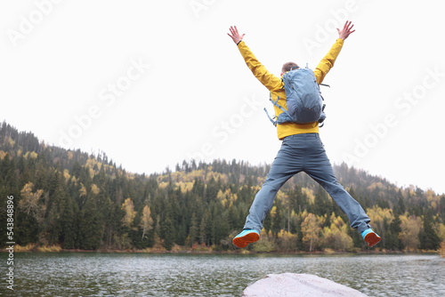 Jumping man in yellow jacket with blue backpack against autumn natire background photo