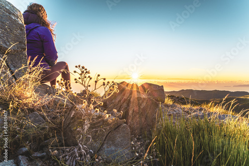 Sitting woman watching the sunrise over the beautiful mountain landscape of Pico do Ariero. Pico do Arieiro, Madeira Island, Portugal, Europe.