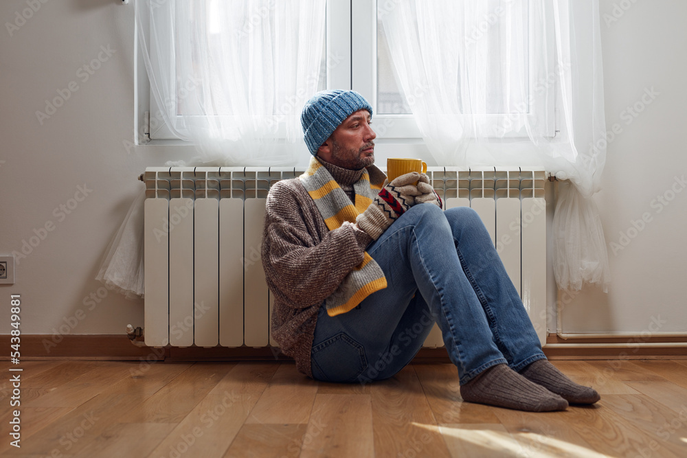Man with hat, sweater and hand gloves indoors on a chilly winter day, energy and gas crisis, cold room, heating problems. Man with hat, sweater and hand gloves indoors on a chilly winter day, energy and gas crisis, cold room, heating problems.