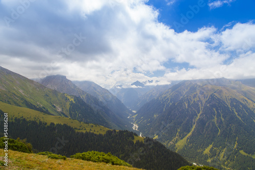 Mountain summer landscape. Snowy mountains and green grass. Peak Karakol Kyrgyzstan. Beautiful view from the top of the mountain
