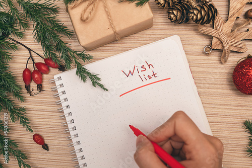 A woman writing a wish list in a notebook, hands close-up, top view.Holiday decorations.New Year and Christmas concept.Planning concept.