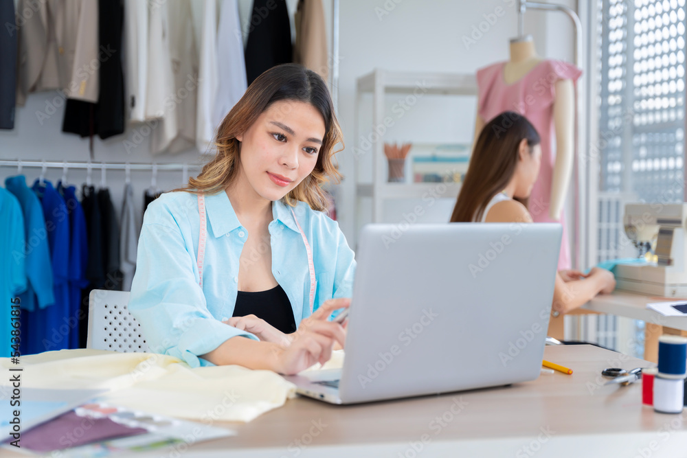 Asian female clothing designers Thailand communicating with customers through laptops in their home office. Showing various color patterns for customers to choose from cut dress as the customer wants. Asian female clothing designers Thailand communicating with customers through laptops in their home office. Showing various color patterns for customers to choose from cut dress as the customer wants.