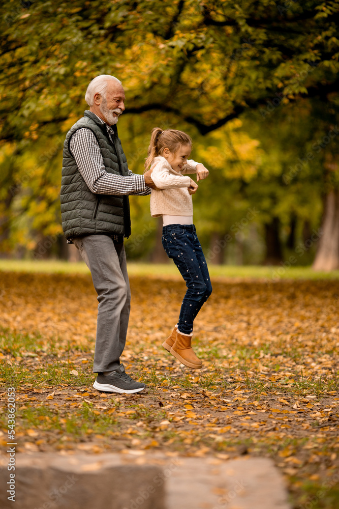Grandfather spending time with his granddaughter in park on autumn day Grandfather spending time with his granddaughter in park on autumn day