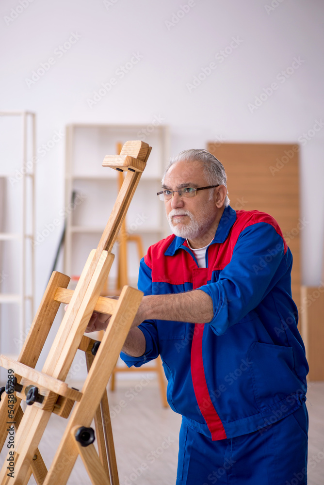 Old male carpenter repairing drawing easel Old male carpenter repairing drawing easel