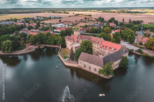 Photography a large lake with a castle in the middle of it and a town in the background with a fountain in the middle