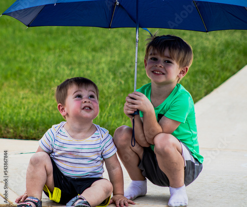 Fotografía two cute young children, brothers boys under umbrella during rain protecting you