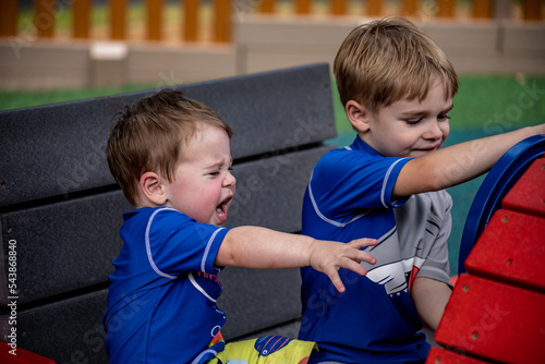Younger brother throwing tantrum while older brother plays on playground equipment