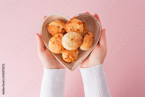 Cheese bread (brazilian Pao de Queijo mineiro) and coffee, heart-shaped plate, woman's hand, top view flat lay photo