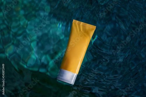 Skin hydration. Yellow tube of cream with a mockup in the blue transparent water. Skin care and hydration concept. photo