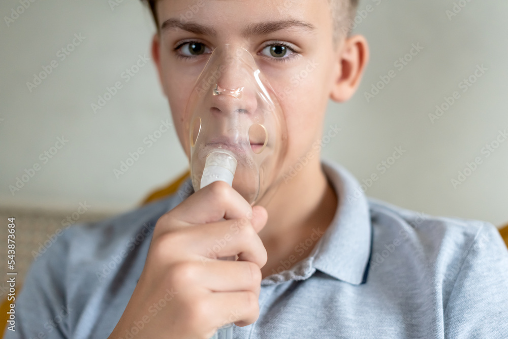 Sick teen boy with an inhaler. Unhealthy child doing inhalation at home, she use nebulizer and inhaler for the treatment, sitting on the couch at home. Asthma inhaler, nebulizer steam, flu or cold Sick teen boy with an inhaler. Unhealthy child doing inhalation at home, she use nebulizer and inhaler for the treatment, sitting on the couch at home. Asthma inhaler, nebulizer steam, flu or cold