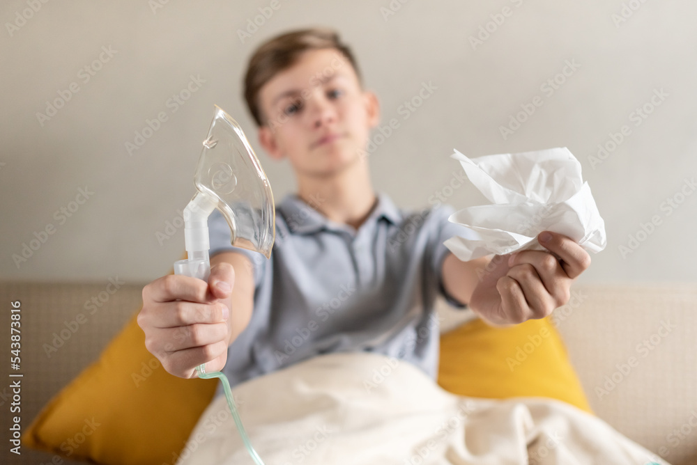 Sick teen boy with an inhaler. Unhealthy child doing inhalation at home, she use nebulizer and inhaler for the treatment, sitting on the couch at home. Asthma inhaler, nebulizer steam, flu or cold Sick teen boy with an inhaler. Unhealthy child doing inhalation at home, she use nebulizer and inhaler for the treatment, sitting on the couch at home. Asthma inhaler, nebulizer steam, flu or cold