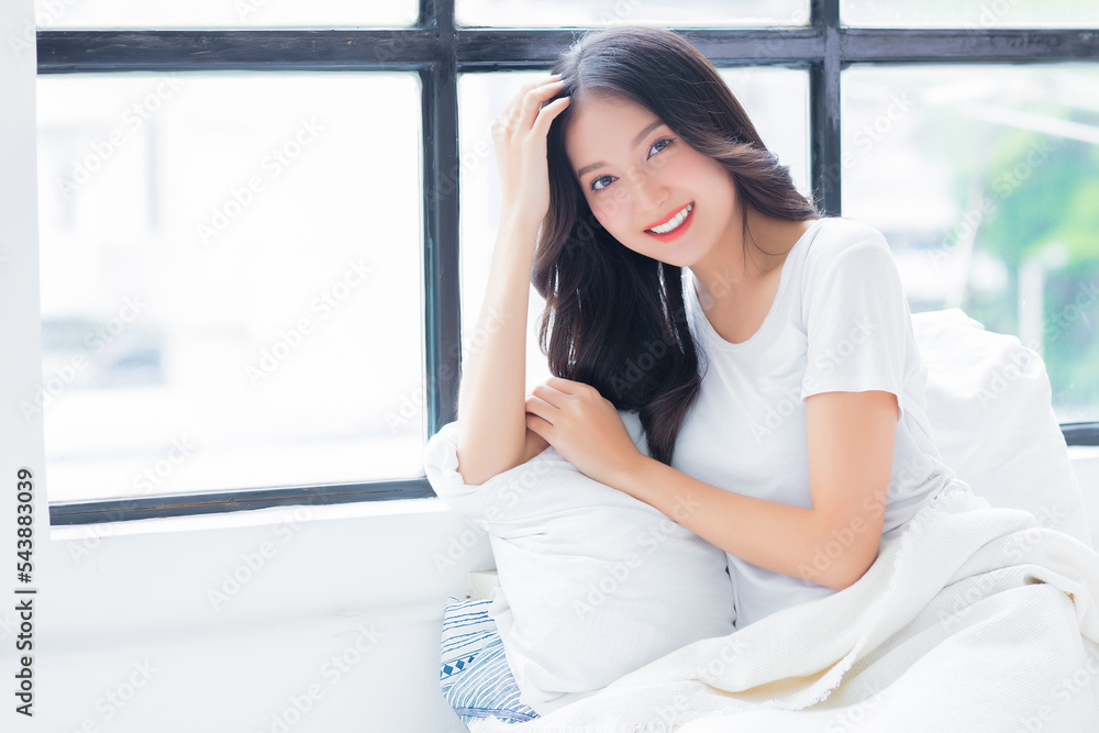Happy fresh relaxed young asian woman resting Pretty lady sit in bed Beautiful girl enjoying good morning after wakeup at home in cozy bedroom She looking at camera stay alone at home with smile face