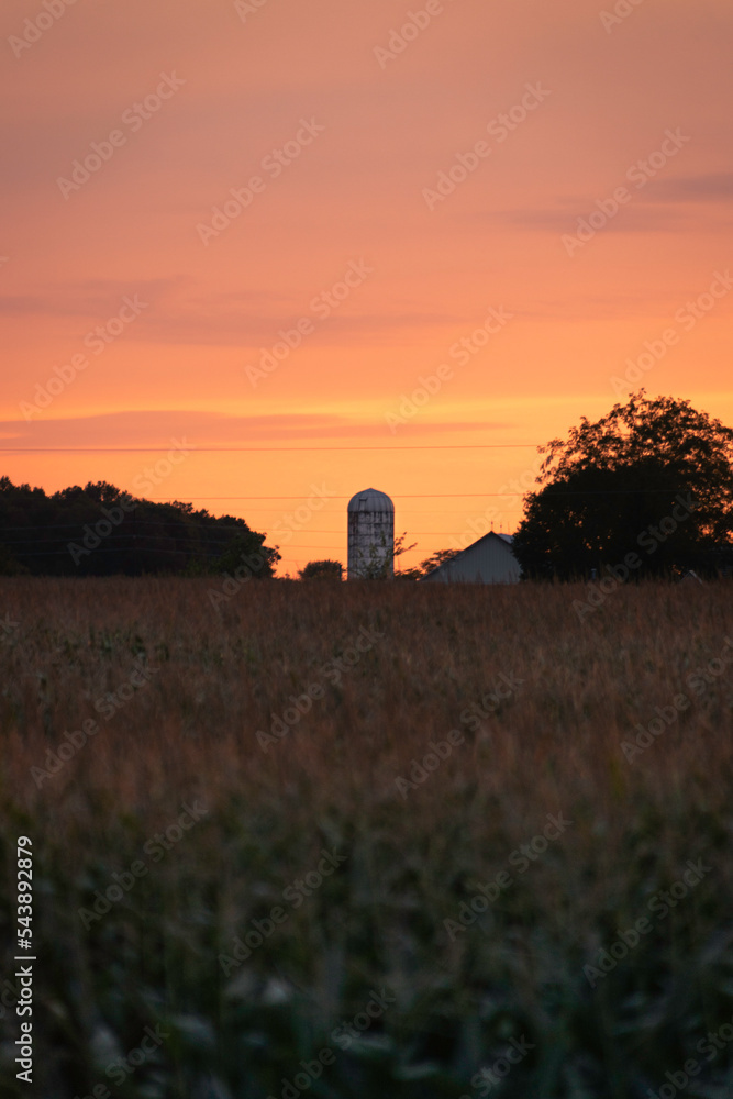 sunset over a field with silos in the distance