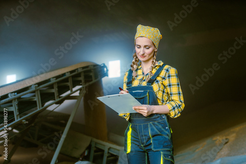 Farmer woman in the granary keeping track of the harvest by taking notes on clipboard