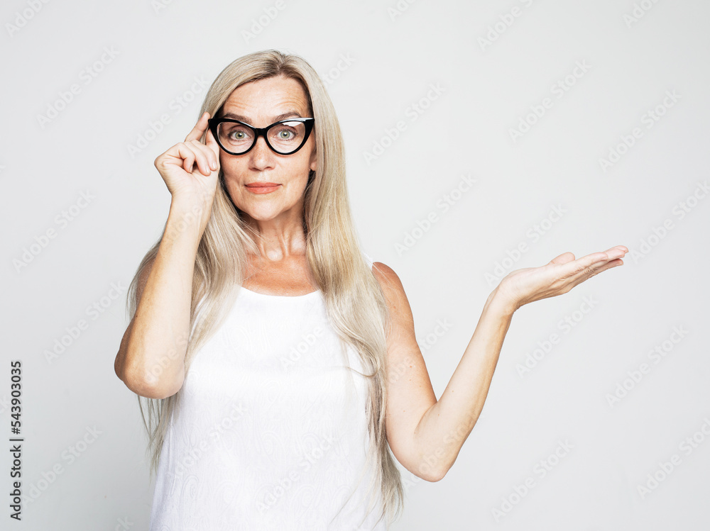 Portrait of perfect old impressed woman in white t-shirt demonstrate, looking, pointing with fingers up to copy space standing over light gray backgroun Portrait of perfect old impressed woman in white t-shirt demonstrate, looking, pointing with fingers up to copy space standing over light gray backgroun