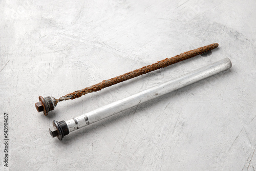 New and old magnesium anode to protect an electric water heater from rust on a gray concrete background, close-up.
