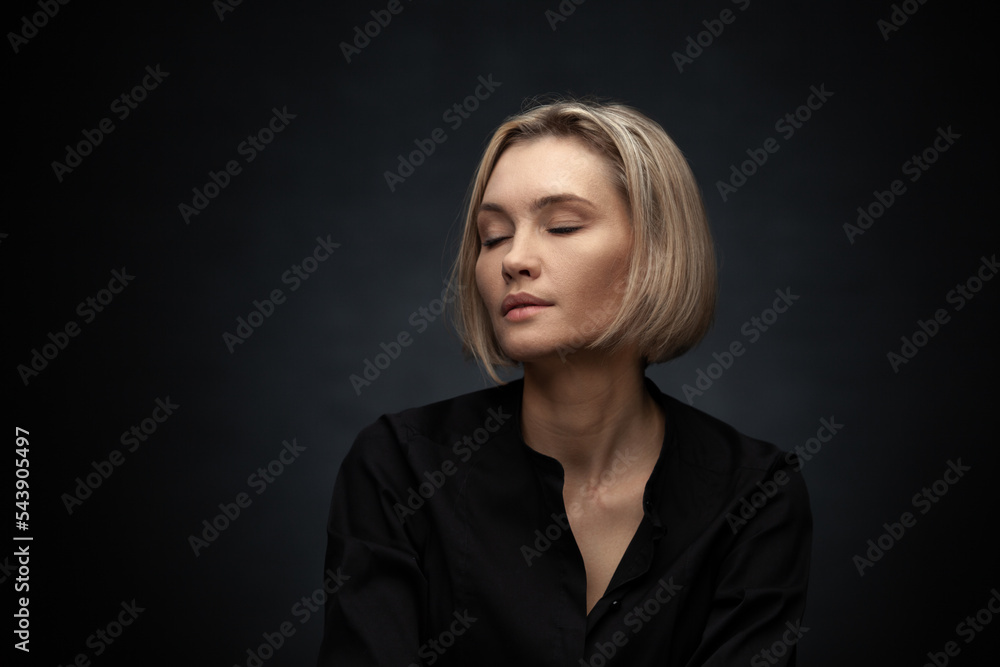 Fototapeta premium Beautiful middle-aged woman on a gray background in a black blouse.