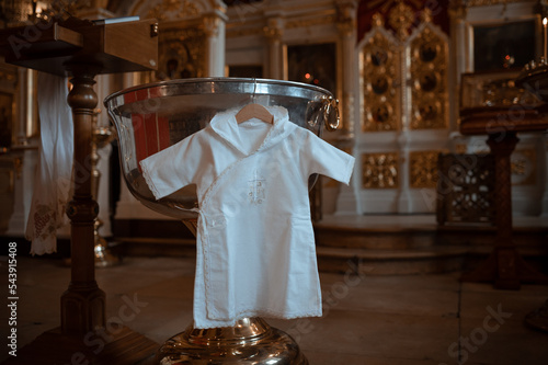 Fototapeta beautiful white traditional baptismal dress near the font for infant baptism