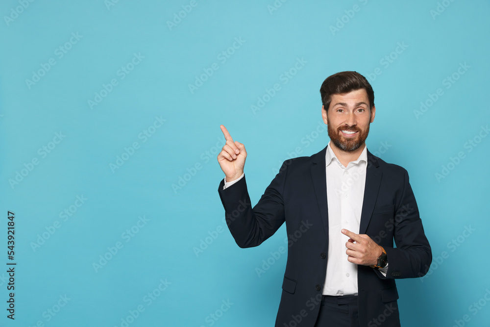 Smiling bearded man pointing index finger up on light blue background. Space for text Smiling bearded man pointing index finger up on light blue background. Space for text