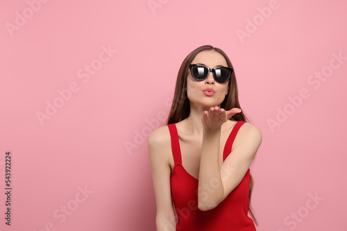 Beautiful young woman with sunglasses blowing kiss on pink background, space for text © New Africa