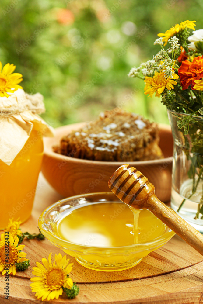 Delicious honey flowing down from dipper into bowl on wooden board in garden Delicious honey flowing down from dipper into bowl on wooden board in garden