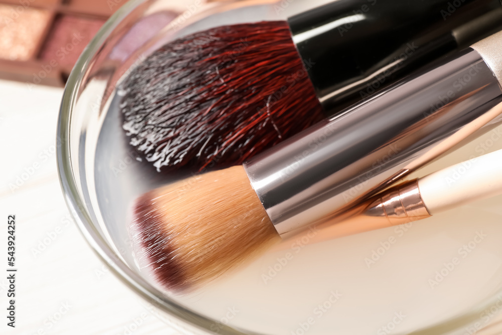 Cleaning makeup brushes in bowl with special liquid on white wooden table, closeup Cleaning makeup brushes in bowl with special liquid on white wooden table, closeup
