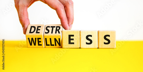 Destress for wellness symbol. Concept words Destress and Wellness on wooden cubes. Businessman hand. Beautiful yellow table white background. Business destress for wellness concept. Copy space.