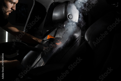 Process of steam cleaning leather seat in car. Worker in auto cleaning service clean car inside. Car interior detailing. © Rabizo Anatolii