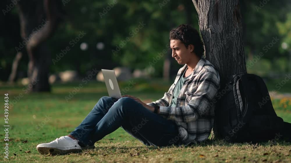 Indian male freelancer student working e learning laptop chatting online outdoor summer sunny park Indian male freelancer student working e learning laptop chatting online outdoor summer sunny park