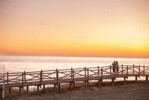 Personas abrazadas contemplando un atardecer en una playa de Málaga.