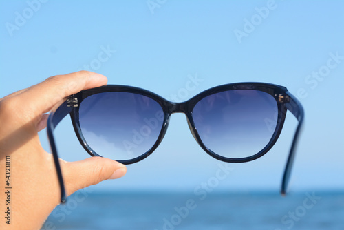 Woman holding stylish sunglasses near sea, closeup