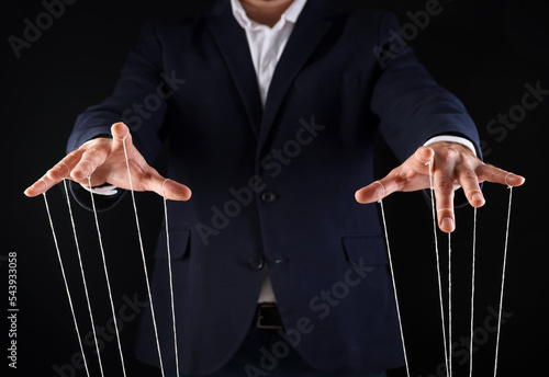 Photo Man in suit pulling strings of puppet on black background, closeup